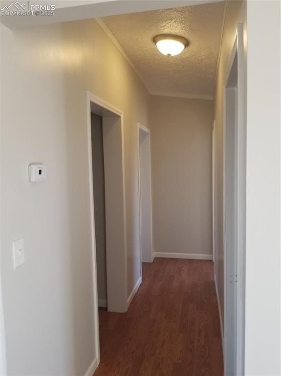 hall featuring dark wood-type flooring, ornamental molding, a textured ceiling, and baseboards