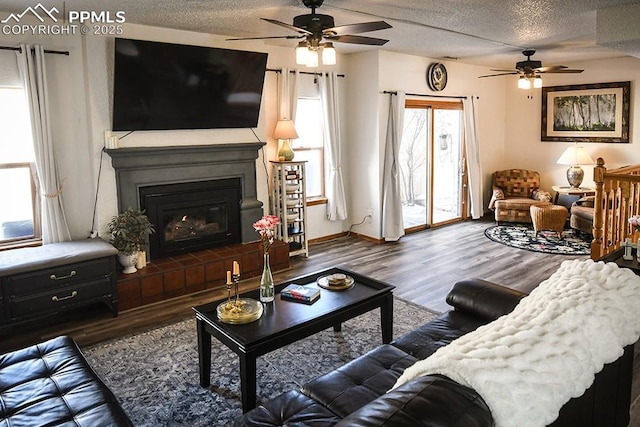 living room featuring baseboards, dark wood finished floors, a textured ceiling, and a glass covered fireplace