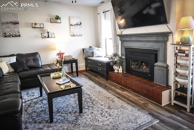 living room featuring a tiled fireplace, baseboards, and dark wood-style flooring