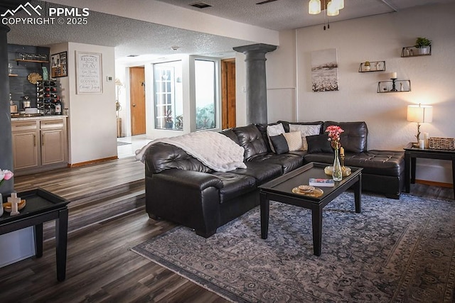 living room with indoor bar, ceiling fan, dark wood-type flooring, a textured ceiling, and ornate columns