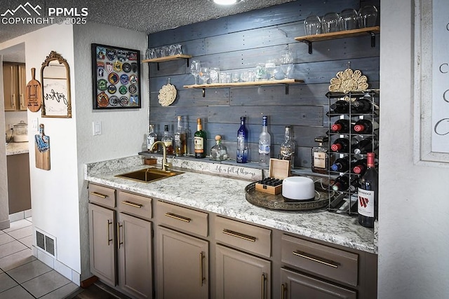 bar featuring indoor wet bar, visible vents, a sink, wooden walls, and tile patterned floors