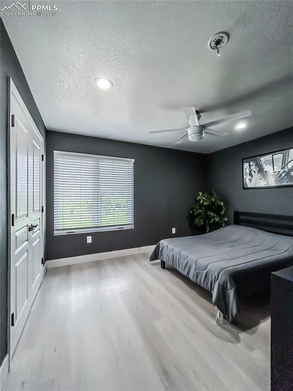 bedroom featuring baseboards, ceiling fan, a textured ceiling, and light wood-style floors