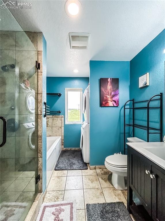 full bathroom featuring toilet, a stall shower, stacked washer / dryer, a textured ceiling, and a bath