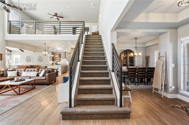 stairway featuring ceiling fan with notable chandelier, baseboards, and wood finished floors