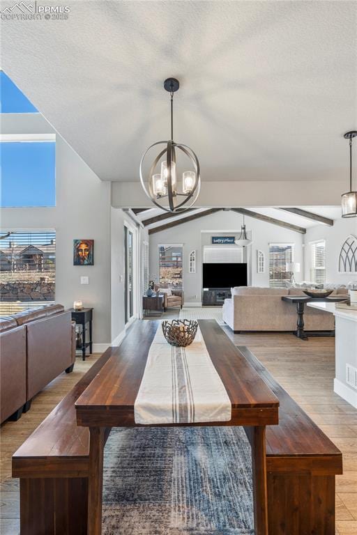 dining room featuring a fireplace, light wood finished floors, an inviting chandelier, vaulted ceiling, and a textured ceiling