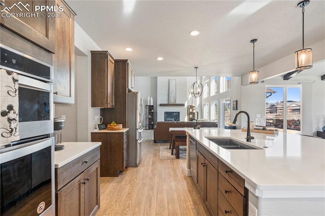 kitchen featuring a glass covered fireplace, a spacious island, open floor plan, light countertops, and a sink