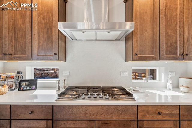 kitchen with light countertops, ventilation hood, brown cabinets, and stainless steel gas stovetop