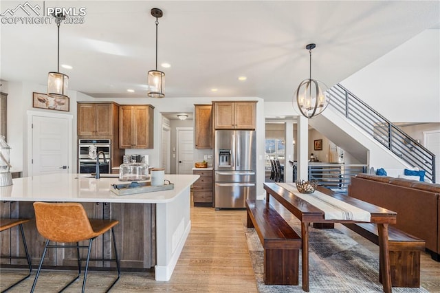 kitchen with light wood finished floors, brown cabinets, stainless steel appliances, light countertops, and pendant lighting