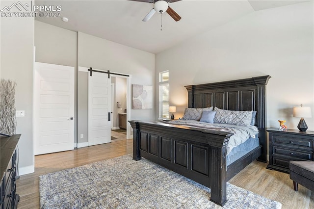 bedroom with ensuite bathroom, a barn door, ceiling fan, wood finished floors, and baseboards