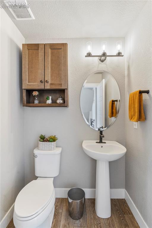 half bath with visible vents, a textured ceiling, toilet, and wood finished floors