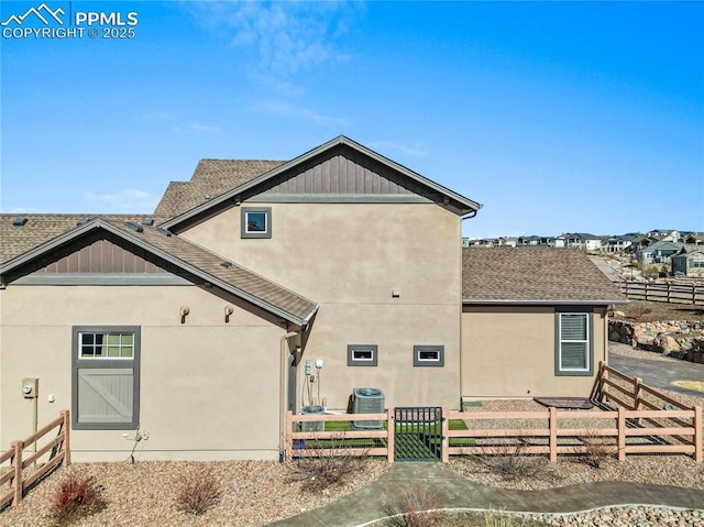 rear view of property with a shingled roof, fence, central AC, and stucco siding