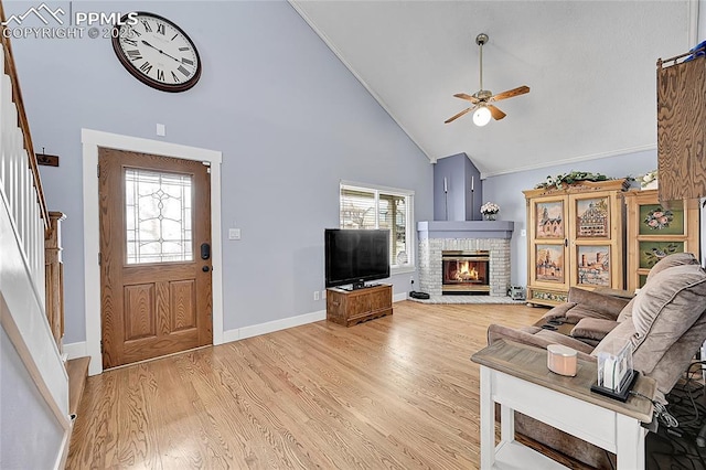 living area featuring stairway, high vaulted ceiling, light wood-style flooring, ceiling fan, and a brick fireplace