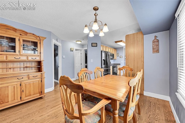 dining area with baseboards, light wood-style floors, an inviting chandelier, and a textured ceiling