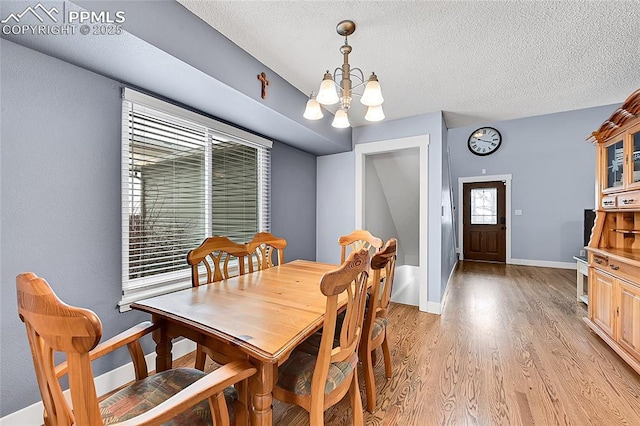 dining room with light wood finished floors, a notable chandelier, a textured ceiling, and baseboards
