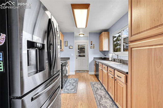 kitchen featuring dark countertops, light wood finished floors, baseboards, stainless steel appliances, and a sink