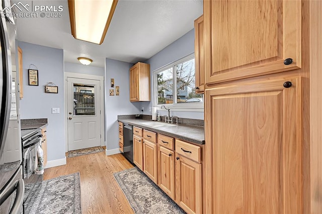 kitchen featuring dark countertops, baseboards, dishwashing machine, light wood-style flooring, and a sink