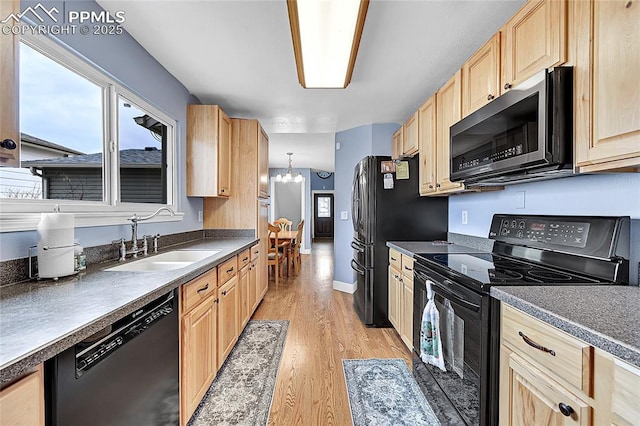 kitchen featuring black appliances, light wood-style flooring, light brown cabinets, a sink, and dark countertops