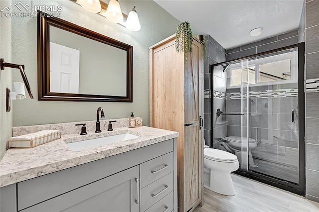 full bathroom featuring a shower stall, toilet, a textured wall, wood finished floors, and vanity