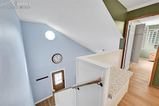 staircase featuring vaulted ceiling, crown molding, plenty of natural light, and wood finished floors