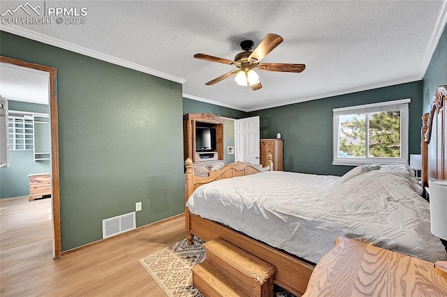 bedroom featuring visible vents, ceiling fan, ornamental molding, wood finished floors, and a textured ceiling