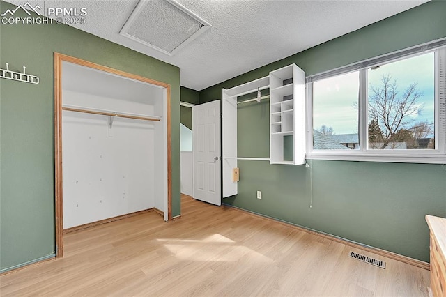 unfurnished bedroom with visible vents, a textured ceiling, attic access, and wood finished floors