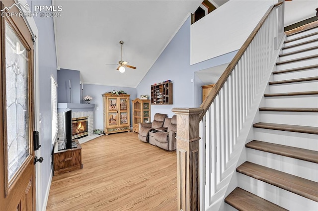 entryway with ceiling fan, stairway, light wood-type flooring, lofted ceiling, and a glass covered fireplace