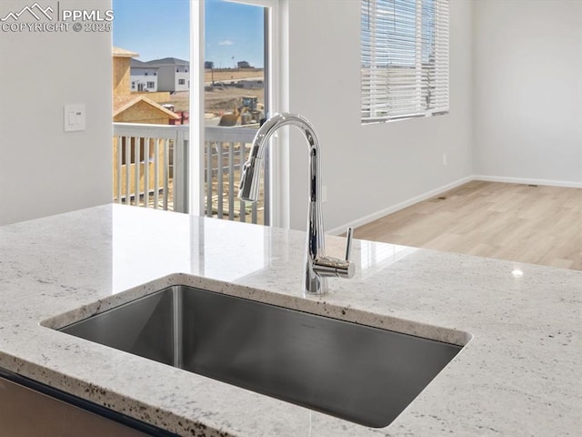 details with baseboards, light stone counters, wood finished floors, and a sink