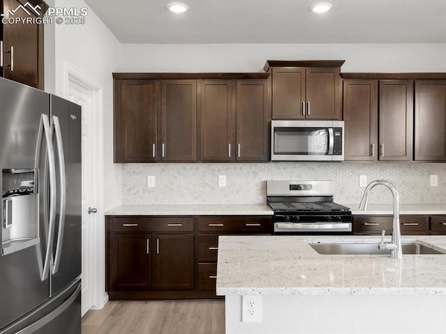 kitchen with dark brown cabinets, light wood-style floors, appliances with stainless steel finishes, and a sink