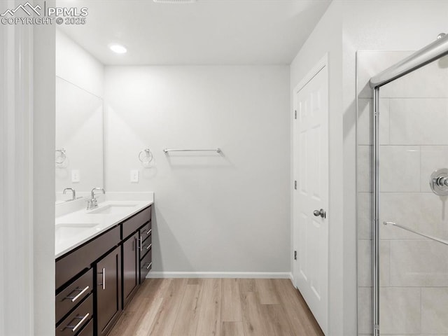 bathroom featuring wood finished floors, a sink, double vanity, and tiled shower