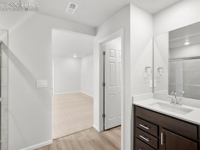 full bathroom featuring wood finished floors, vanity, a tile shower, baseboards, and visible vents