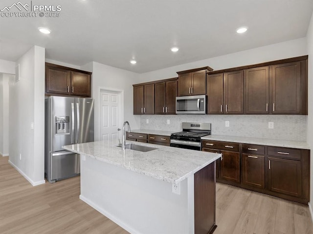 kitchen with dark brown cabinetry, stainless steel appliances, light wood finished floors, and a sink