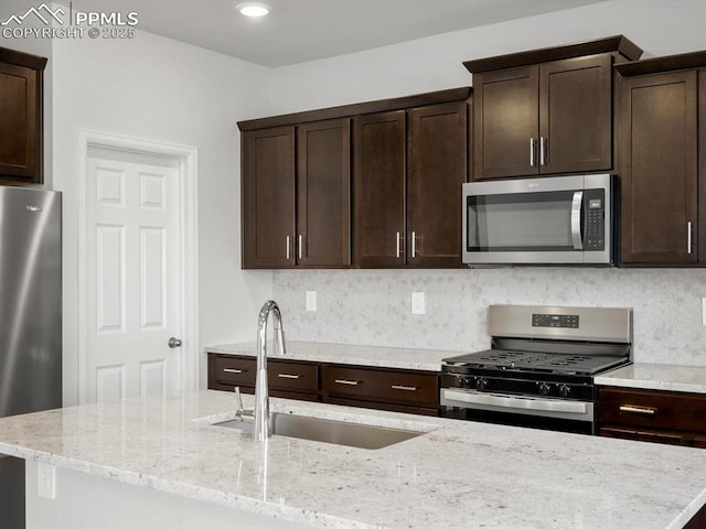 kitchen with dark brown cabinets, stainless steel appliances, decorative backsplash, and a sink