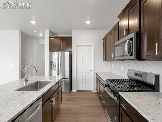 kitchen featuring light stone counters, a sink, light wood-style floors, dark brown cabinetry, and appliances with stainless steel finishes