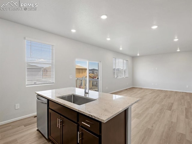 kitchen with a kitchen island with sink, stainless steel dishwasher, a sink, light wood-type flooring, and dark brown cabinetry