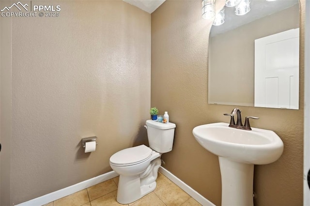 half bathroom featuring toilet, tile patterned flooring, baseboards, and a sink