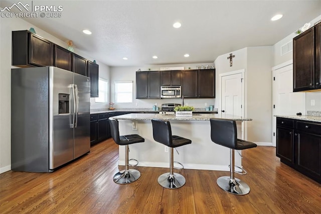 kitchen featuring a breakfast bar, dark wood-style flooring, visible vents, appliances with stainless steel finishes, and light stone countertops