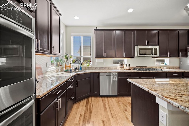 kitchen with light stone countertops, a sink, stainless steel appliances, dark brown cabinetry, and light wood-type flooring