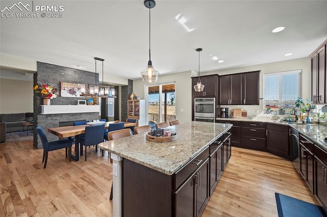 kitchen featuring light stone counters, a kitchen island, dark brown cabinets, light wood-style floors, and appliances with stainless steel finishes