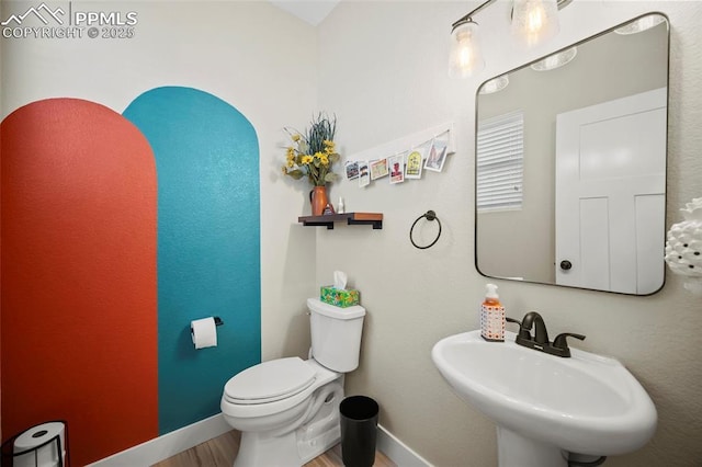 half bathroom featuring toilet, wood finished floors, baseboards, and a sink