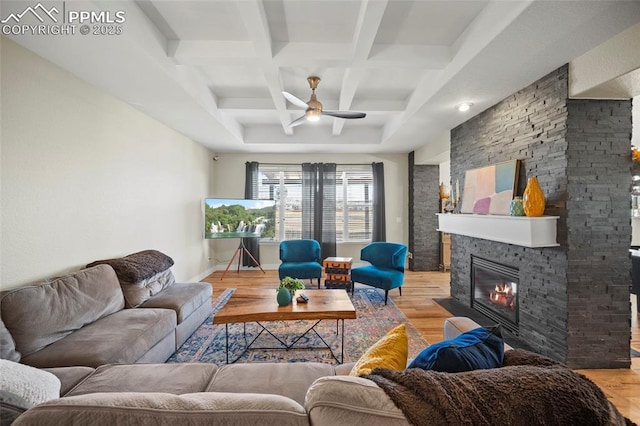 living area featuring light wood-type flooring, beam ceiling, a ceiling fan, coffered ceiling, and a stone fireplace