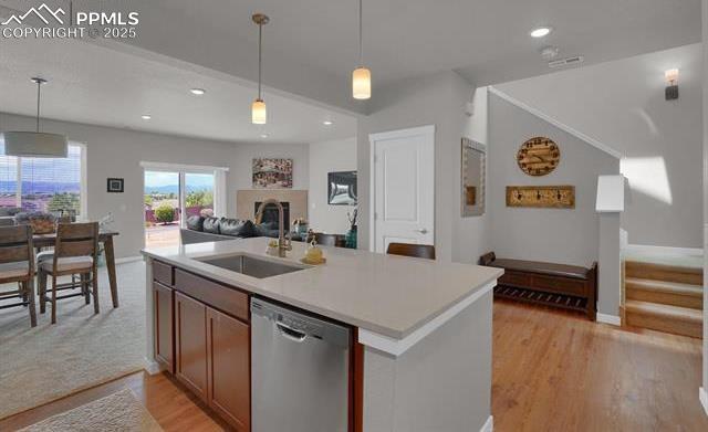 kitchen with a fireplace, a sink, hanging light fixtures, stainless steel dishwasher, and open floor plan