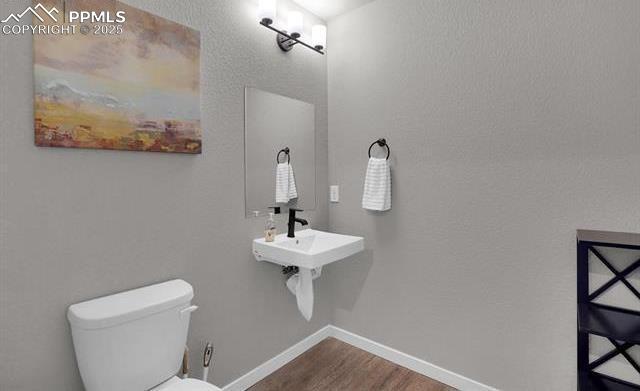 half bathroom featuring toilet, wood finished floors, baseboards, and a sink