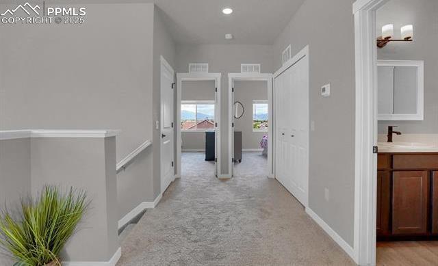 hallway featuring visible vents, light colored carpet, baseboards, and a sink