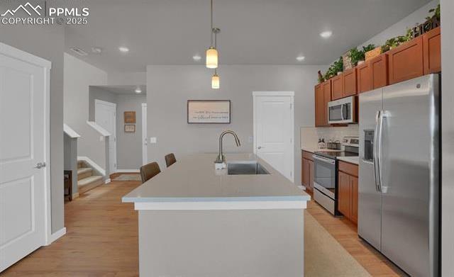 kitchen featuring brown cabinets, appliances with stainless steel finishes, light wood-style flooring, and a sink