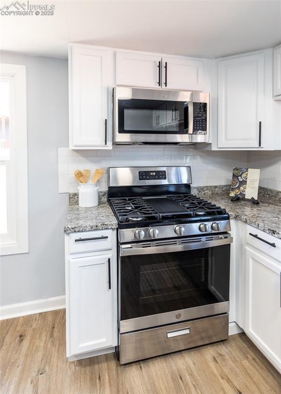 kitchen with baseboards, decorative backsplash, stainless steel appliances, light wood-style floors, and white cabinetry