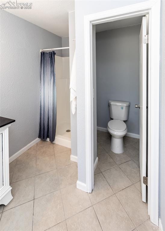 full bath with toilet, a stall shower, baseboards, and tile patterned floors