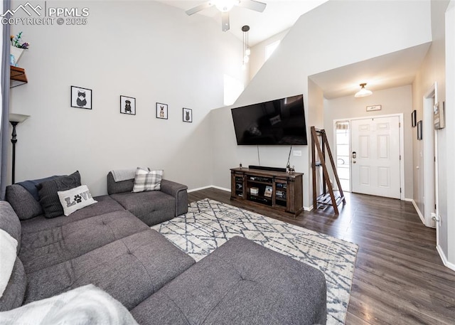 living room with wood finished floors, baseboards, ceiling fan, and a towering ceiling