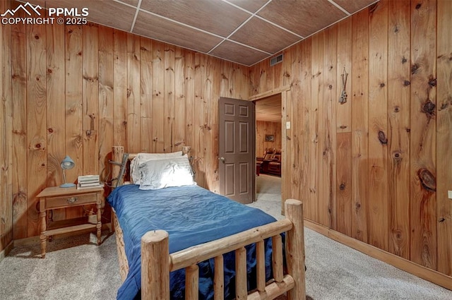 carpeted bedroom featuring wood walls and visible vents