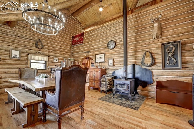 dining area with log walls, a wood stove, wood finished floors, high vaulted ceiling, and beamed ceiling