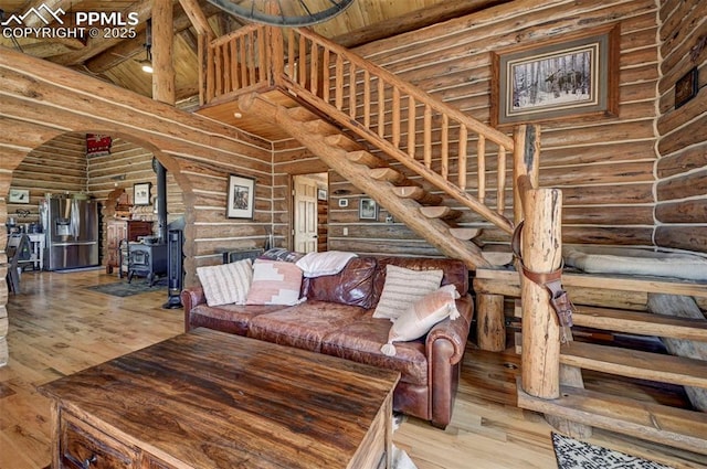 unfurnished living room with a wood stove, stairs, high vaulted ceiling, and wood finished floors